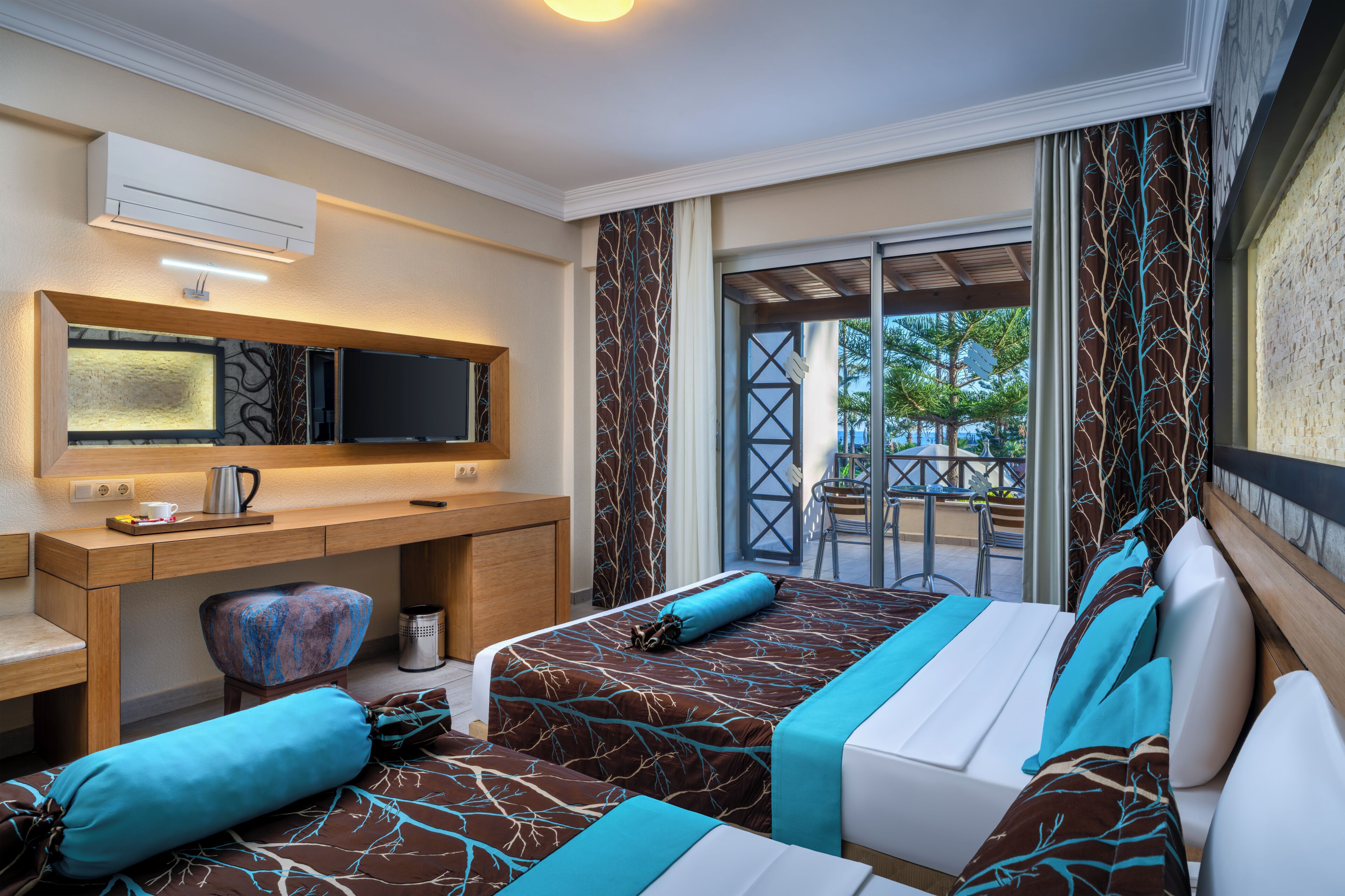 A hotel room with a desk, two beds, a TV, and a balcony with a view.
