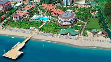 An aerial view of a resort with a beach, a pier, and a large circular building with a pool.