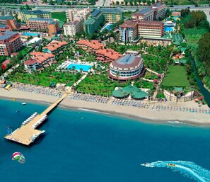 An aerial view of a resort with a beach, a pier, and a large circular building with a pool. - Saphir Hotel & Villas - All inclusive (Alanya)