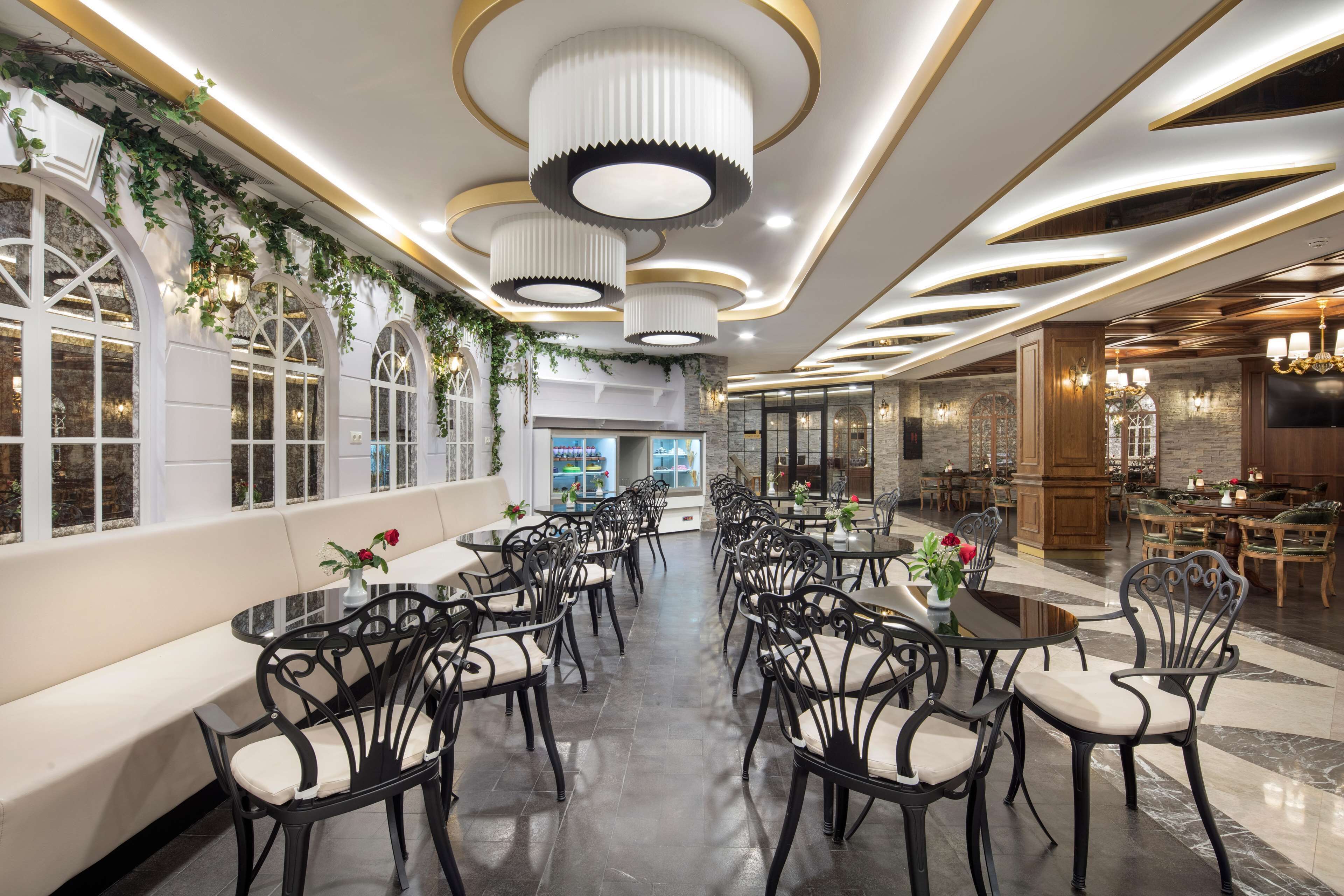 A spacious dining area with round tables and black chairs, a long bench along the wall, and decorative lighting fixtures.