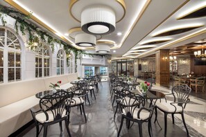 A spacious dining area with round tables and black chairs, a long bench along the wall, and decorative lighting fixtures. - Saphir Hotel & Villas - All inclusive (Alanya)