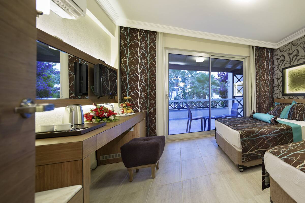 A hotel room with two beds, a desk, a chair, and a large window.