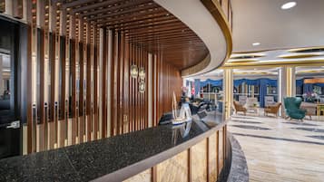 A modern hotel lobby with a curved reception desk, a seating area with plush chairs, and a marble floor.