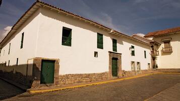 A white building with green doors and windows, a stone base, and a cobblestone street.