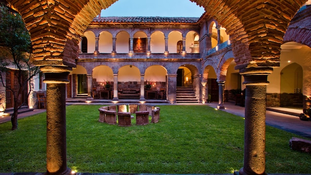 Un patio con una fuente central, rodeado de columnas y arcos de piedra, y un edificio de varios niveles con ventanas.