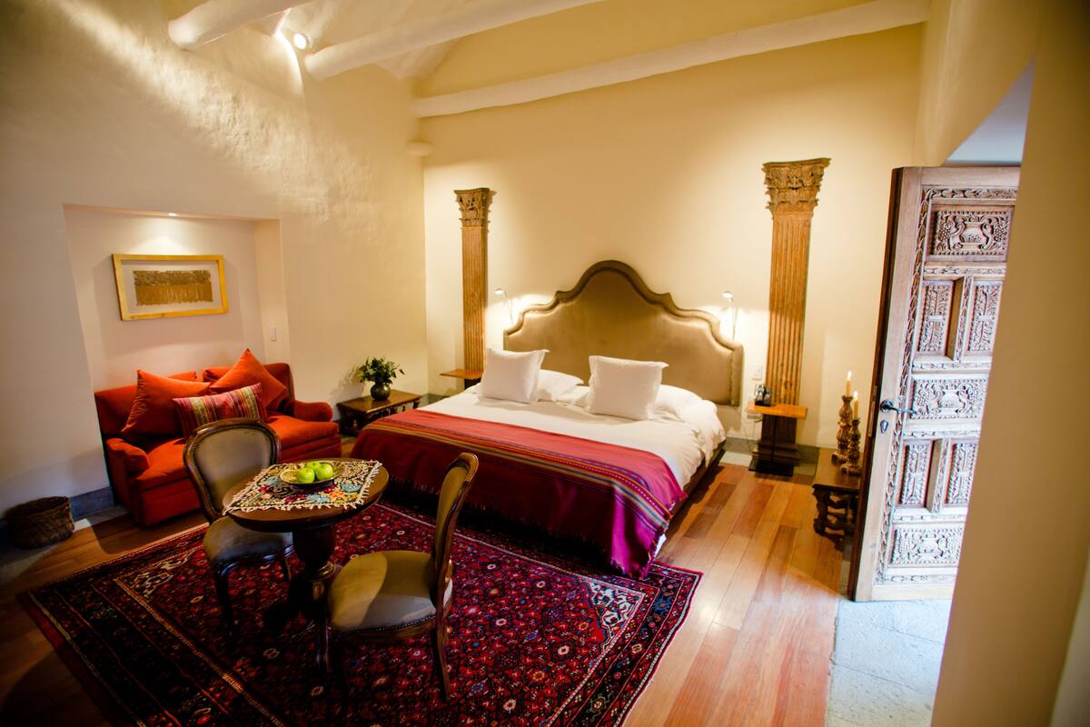 A hotel room with a large bed, a sitting area with a table and chairs, and a decorative door.