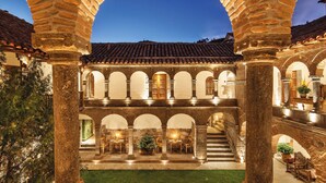 Un patio con arcos de piedra y techo de tejas, con mobiliario exterior y una escalera.