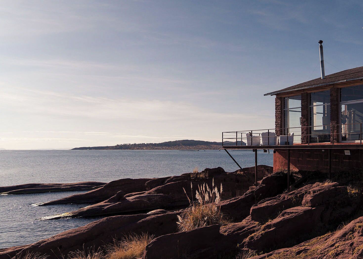 A coastal building with a view of the sea, featuring a balcony with chairs and a table.