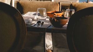 A dining table set with cutlery, a bowl, and glasses, overlooking a coastal view with boats and a rocky island. - Titilaka by Andean (Platería)