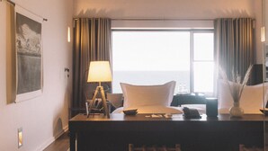 A hotel room with a wooden ceiling, a large window with curtains, a desk with a lamp, a bed with pillows, and a small table with a vase. - Titilaka by Andean (Platería)
