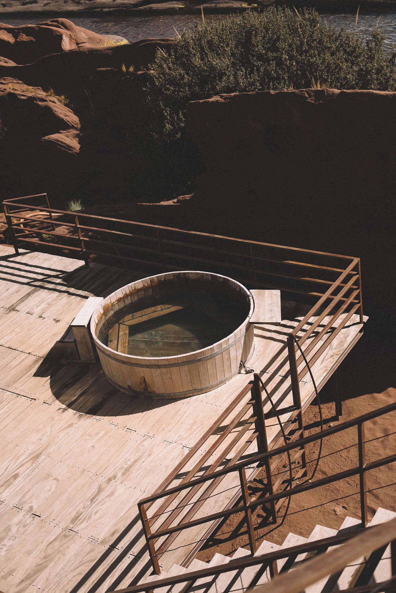 Una bañera de hidromasaje de madera en una terraza con barandas metálicas, rodeada de formaciones rocosas naturales y vegetación.