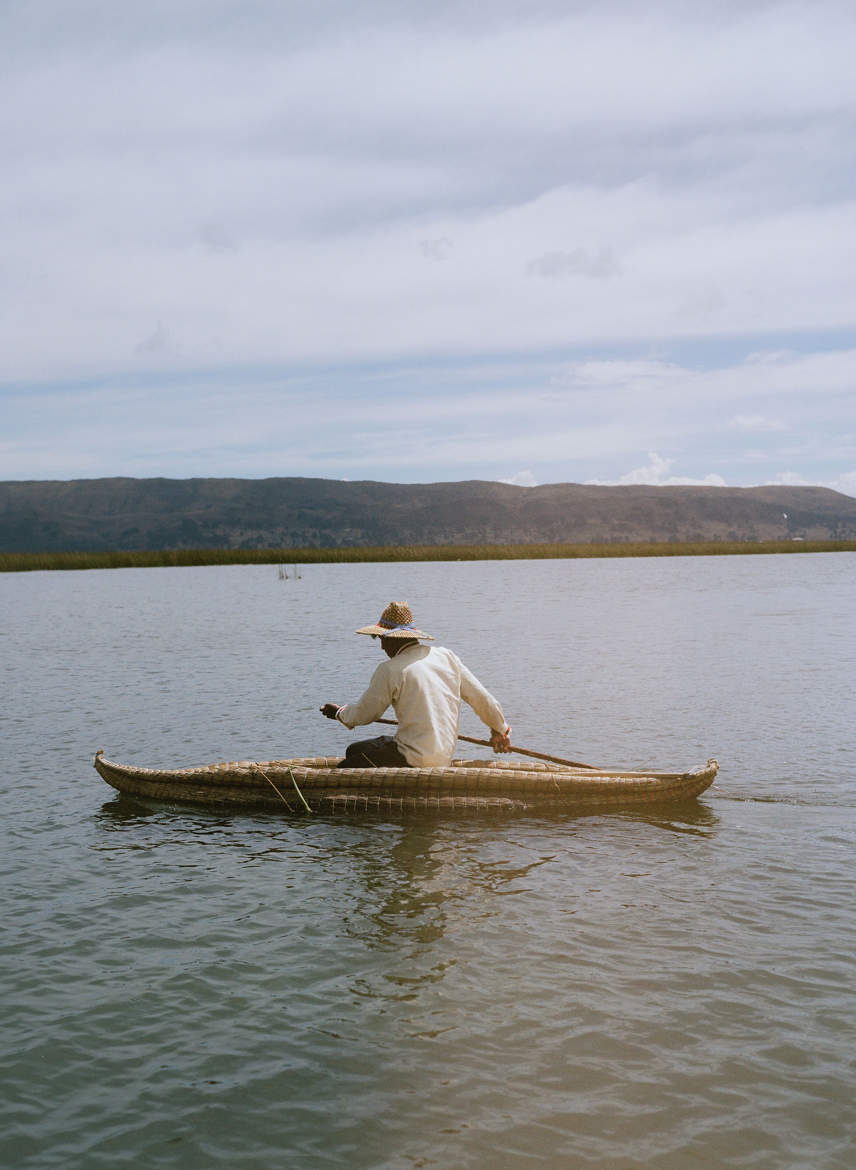 A person in a canoe on a calm body of water with hills in the background.