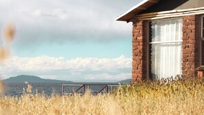 A rustic building with a brick exterior and a large window with white curtains. - Titilaka by Andean (Platería)