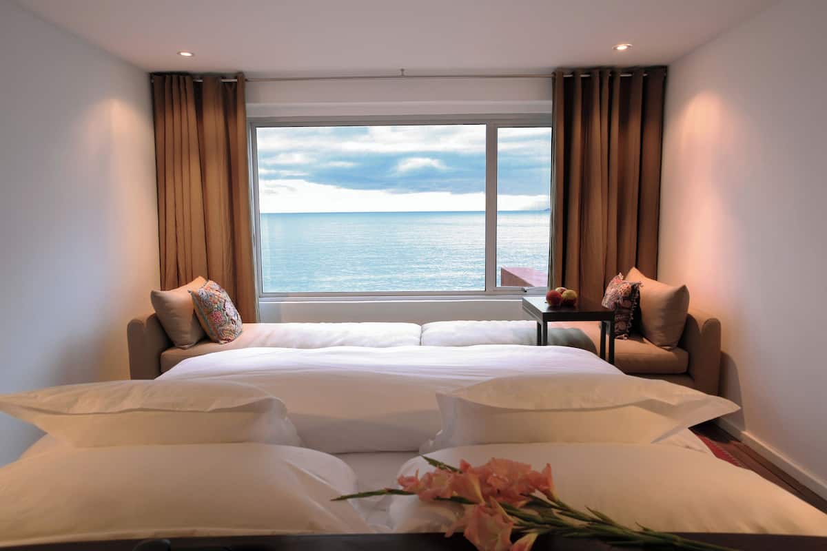 Una habitación de hotel con una cama, dos sillas, una mesita y una ventana con cortinas.