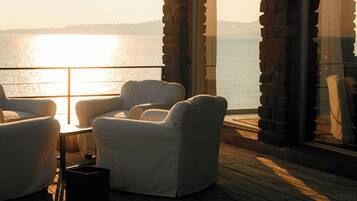 A deck with two white cushioned chairs and a small table, overlooking a body of water.