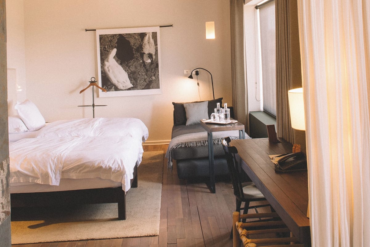 Una habitación de hotel con cama, mesita de noche, lámpara y un cuadro en la pared.