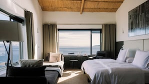 A hotel room with two beds, a desk, a chair, and a large window offering a view of the sea. - Titilaka by Andean (Platería)