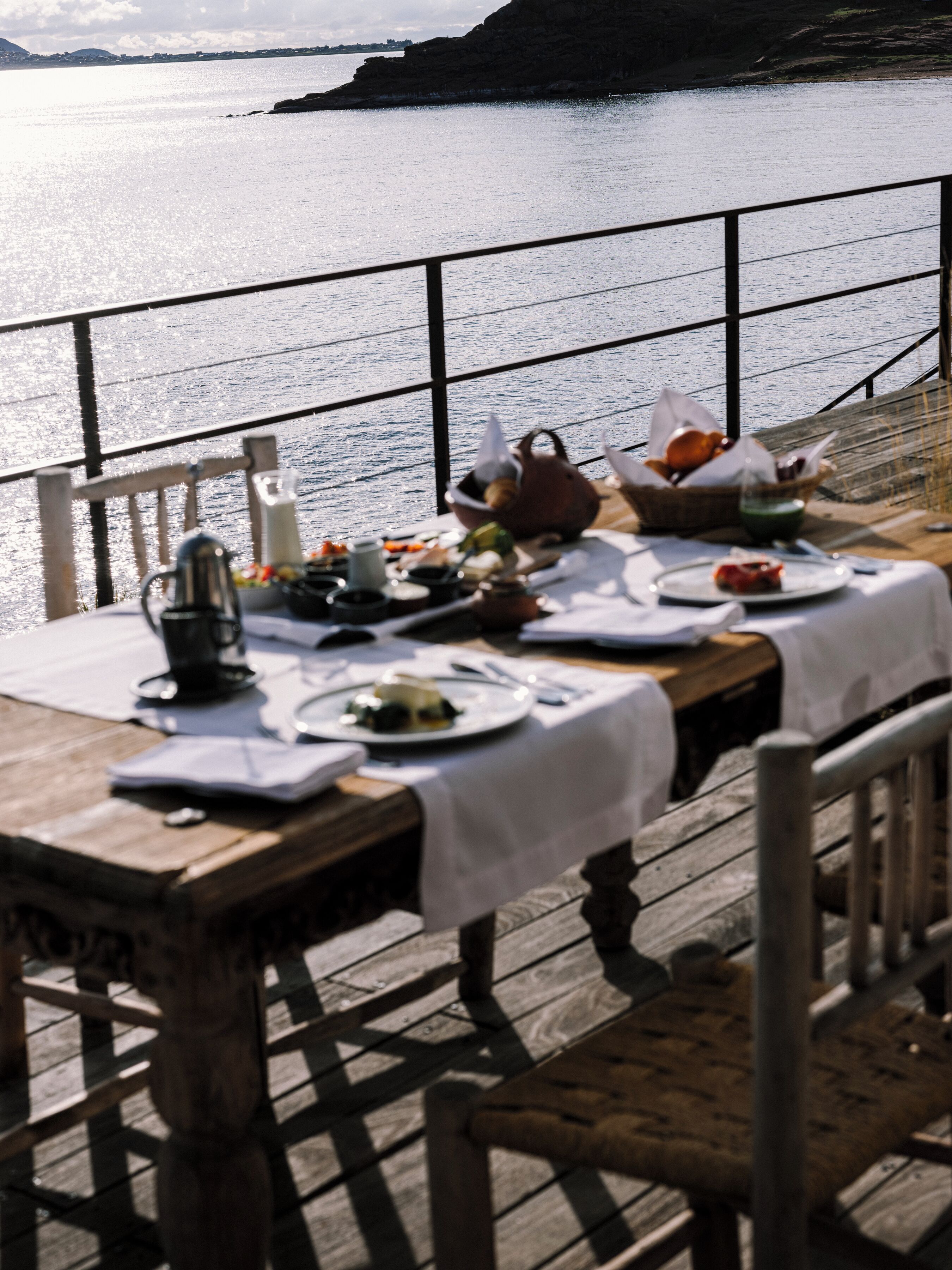 A wooden deck with a table set for a meal, overlooking a body of water.