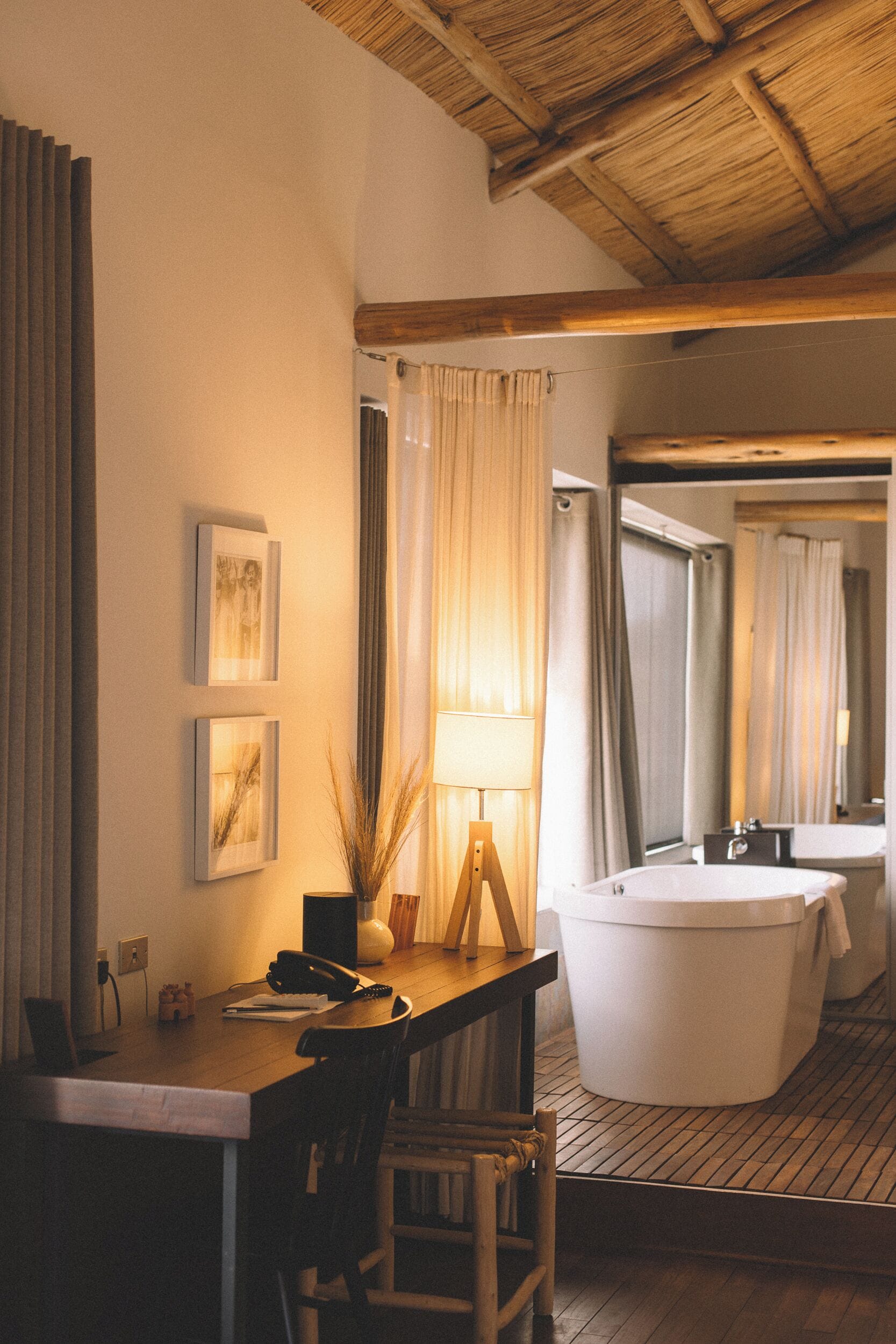 A room with a wooden desk, a telephone, a lamp, and a large bathtub.