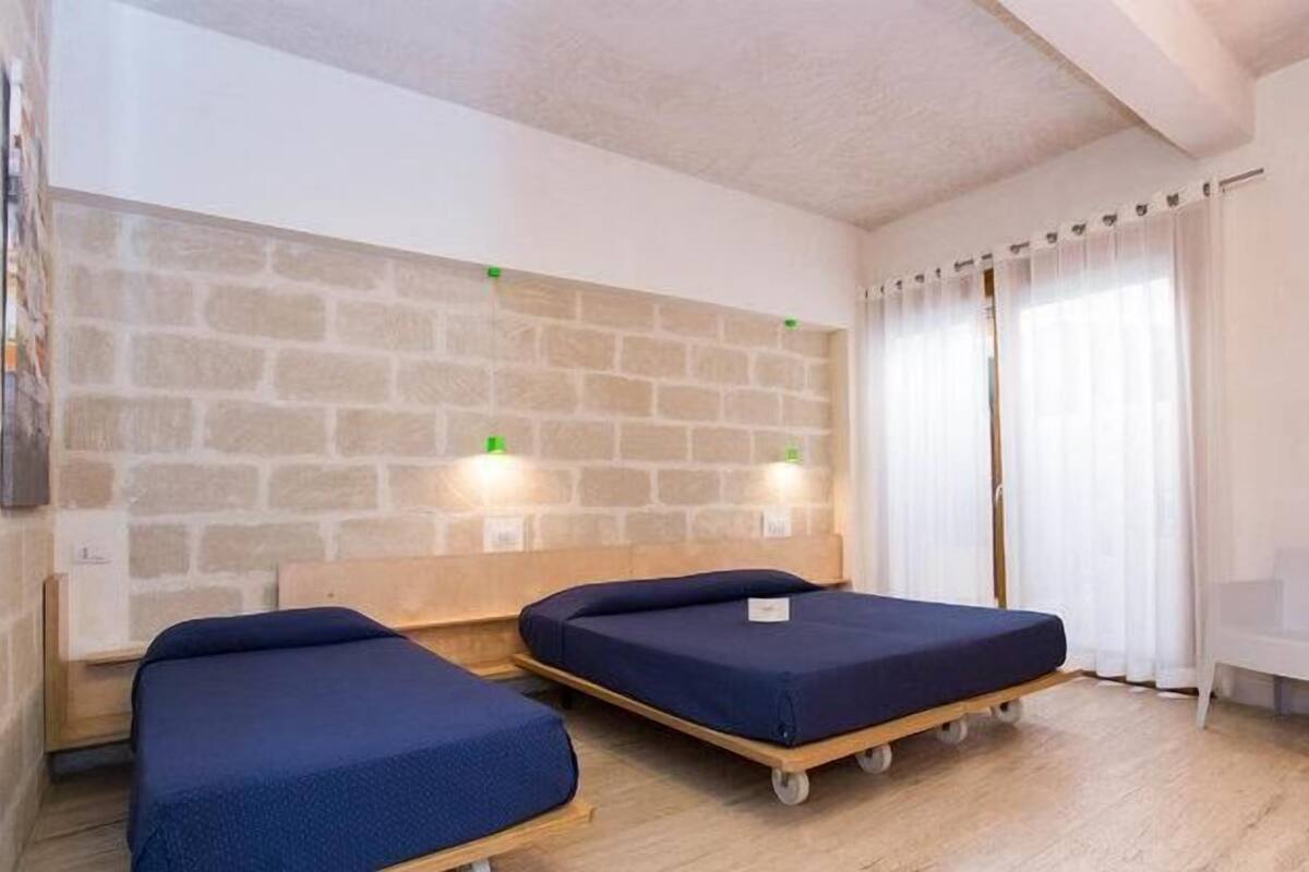 Une chambre avec deux lits, un plancher en bois, des murs en pierre et une chaise blanche.