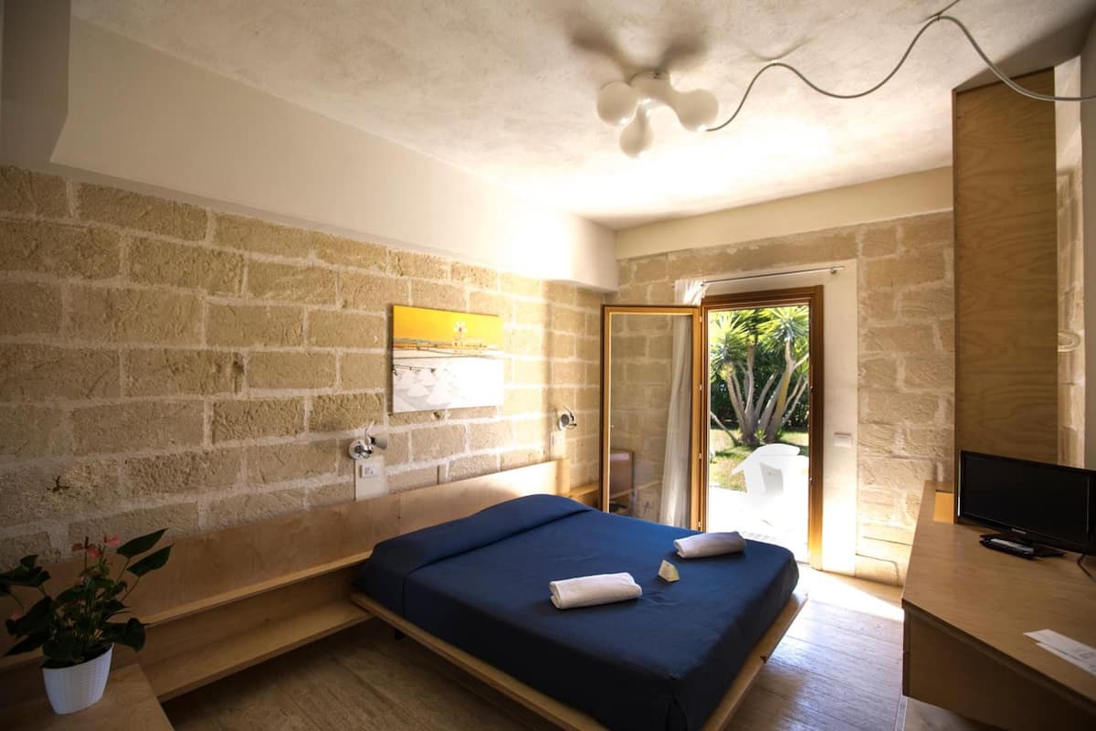 Une chambre à coucher avec un lit, une télévision, une plante et une vue sur un jardin, visible à travers une porte vitrée.