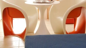A room with two white chairs around a small table, a red cabinet, and a window with curtains. - Cave Bianche Hotel (Favignana)