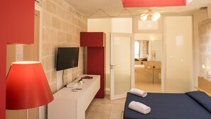 A hotel room with a bed, a TV, a desk, and a mirror. - Cave Bianche Hotel (Favignana)