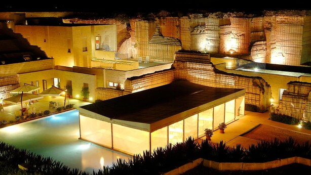 A modern building with a swimming pool, outdoor seating, and a large glass enclosure. - Cave Bianche Hotel (Favignana)
