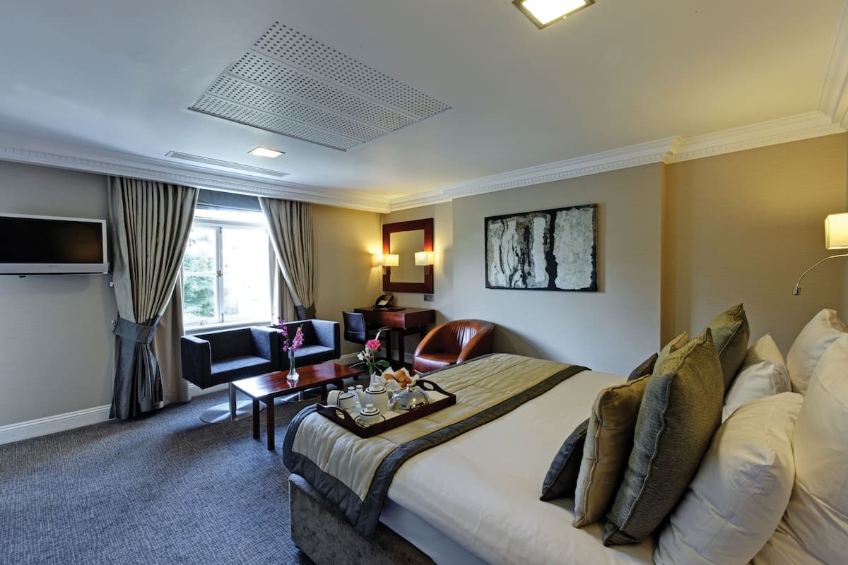 A hotel room with a large bed, a desk with a chair, a TV, and a window with curtains.