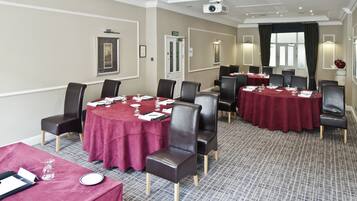 A conference room with multiple tables and chairs, equipped with nameplates, water glasses, and notepads.