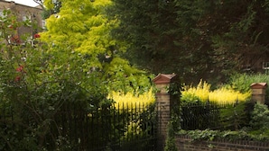 A patio area with metal chairs and tables, surrounded by a brick wall and greenery. - Grange Beauchamp (London)