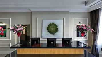 A reception area with a reception desk, three chairs, two vases with flowers, and a framed artwork on the wall.