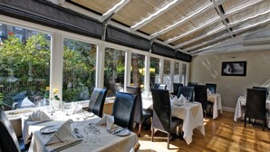 A restaurant with tables set for dining, large windows, and a view of greenery outside. - Grange Beauchamp (London)