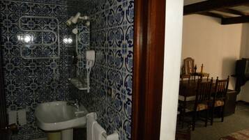 A bathroom with a sink, towel rack, and a shower area with a white hose.