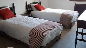 Two single beds with wooden headboards and white bedding, a small table and chair, and a window with an outside view.