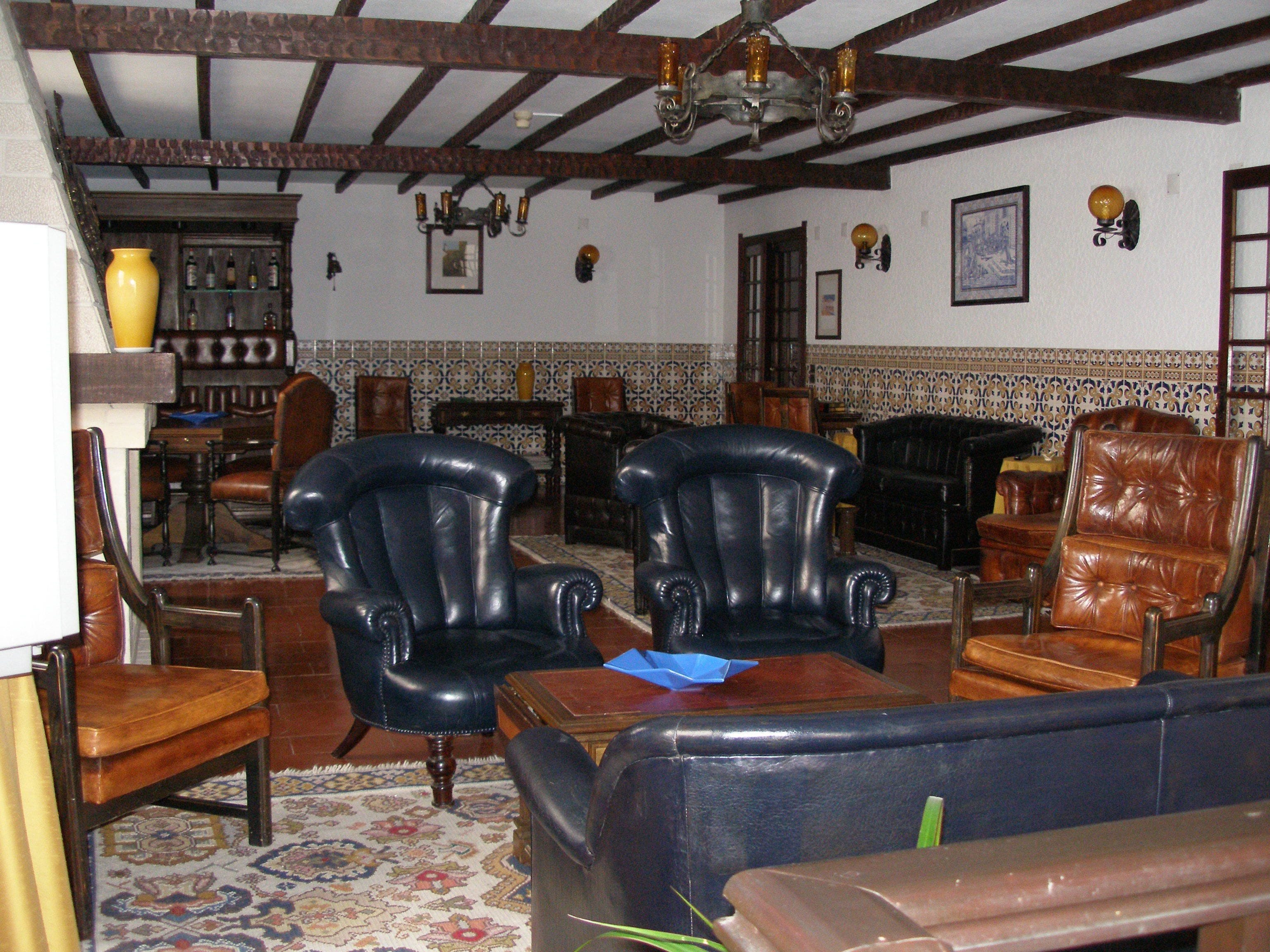 Una habitación tradicional con vigas de madera, sillones de cuero, un tapete estampado y una araña.