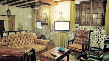 A room with a leather sofa, a wooden coffee table, a television, and patterned wallpaper.