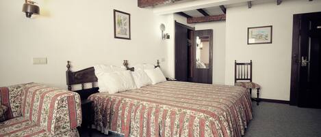 A room with two beds, wooden beams on the ceiling, a small table, and a chair.