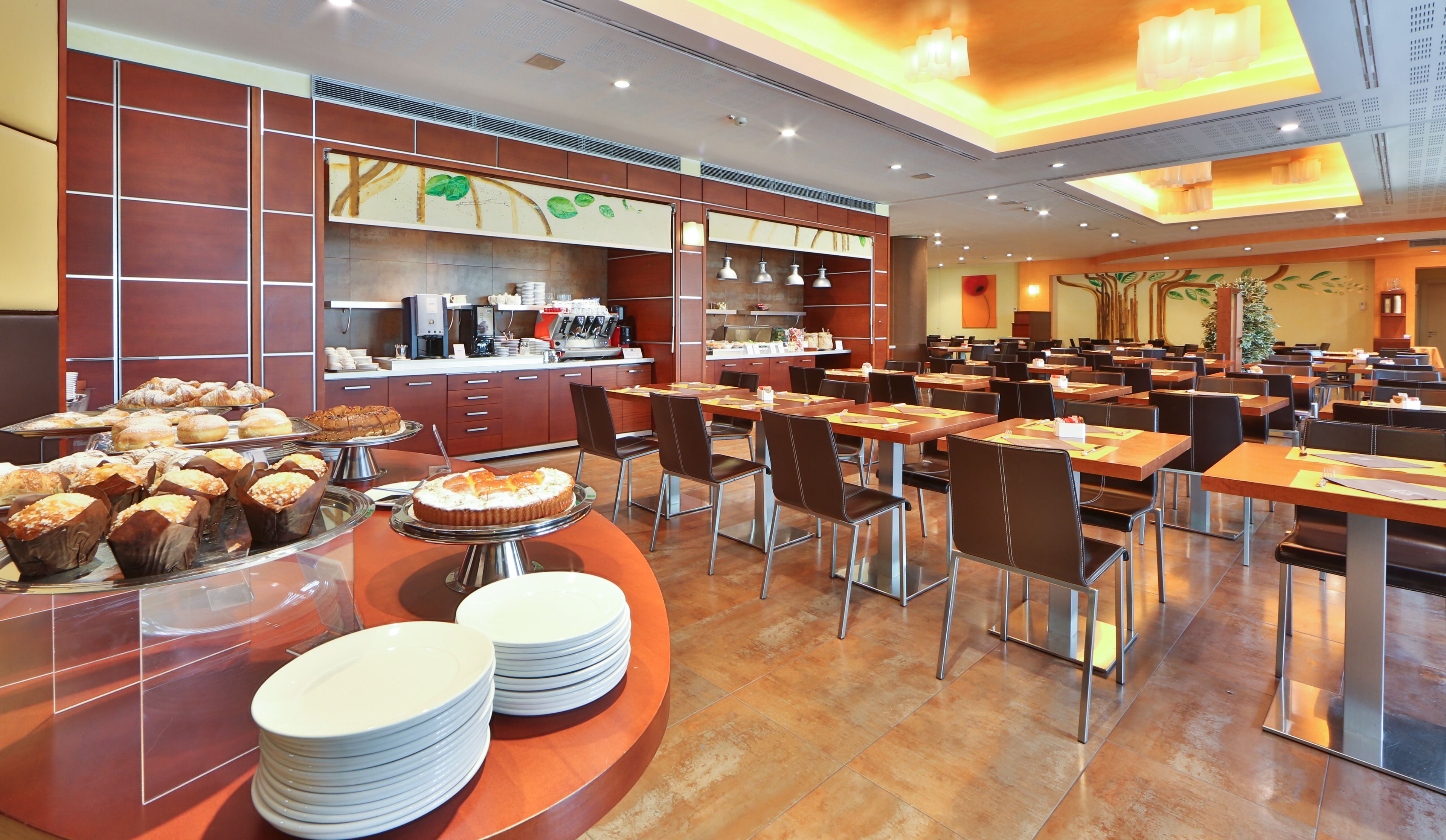 Un comedor amplio con varias mesas y sillas, una barra de buffet con distintos alimentos, y una zona de cocina al fondo.