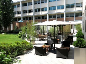 An outdoor patio with wicker furniture, umbrellas, and potted plants.
