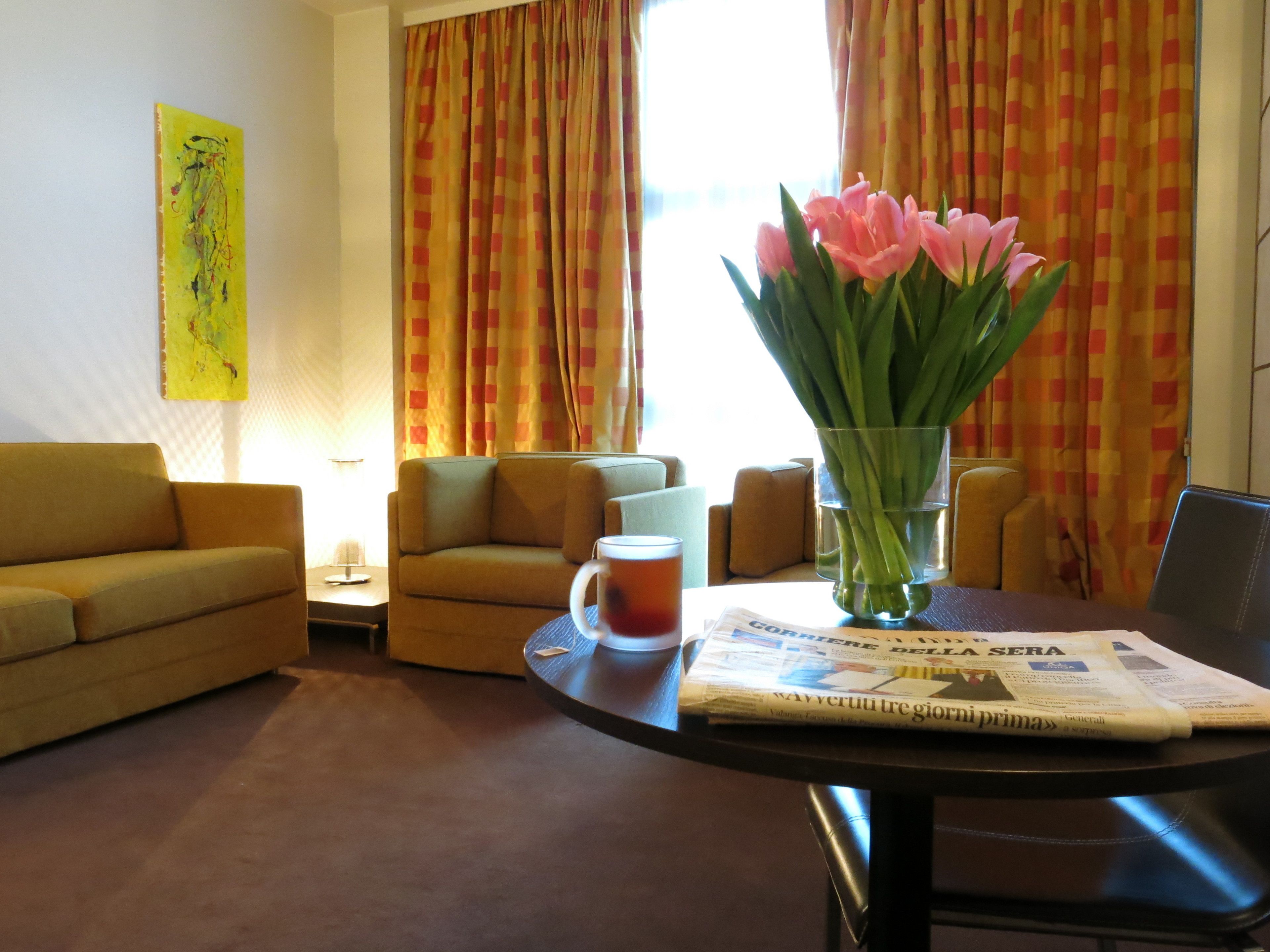 A living room with a sofa, armchairs, a coffee table with a newspaper, and a vase with flowers.