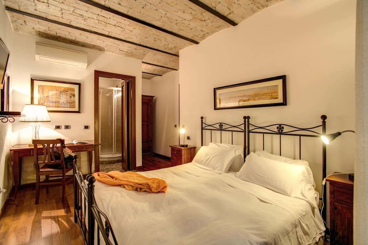 A bedroom with a bed, a desk, a chair, a nightstand, and a lamp.