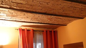 A room with exposed wooden beams on the ceiling, a window with red curtains, and a plain wall. - Residenza Domizia- Guest House (Rome)