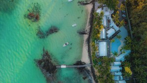 Vista aérea de un complejo turístico con playa, muelle y zona de piscina rodeada de palmeras.