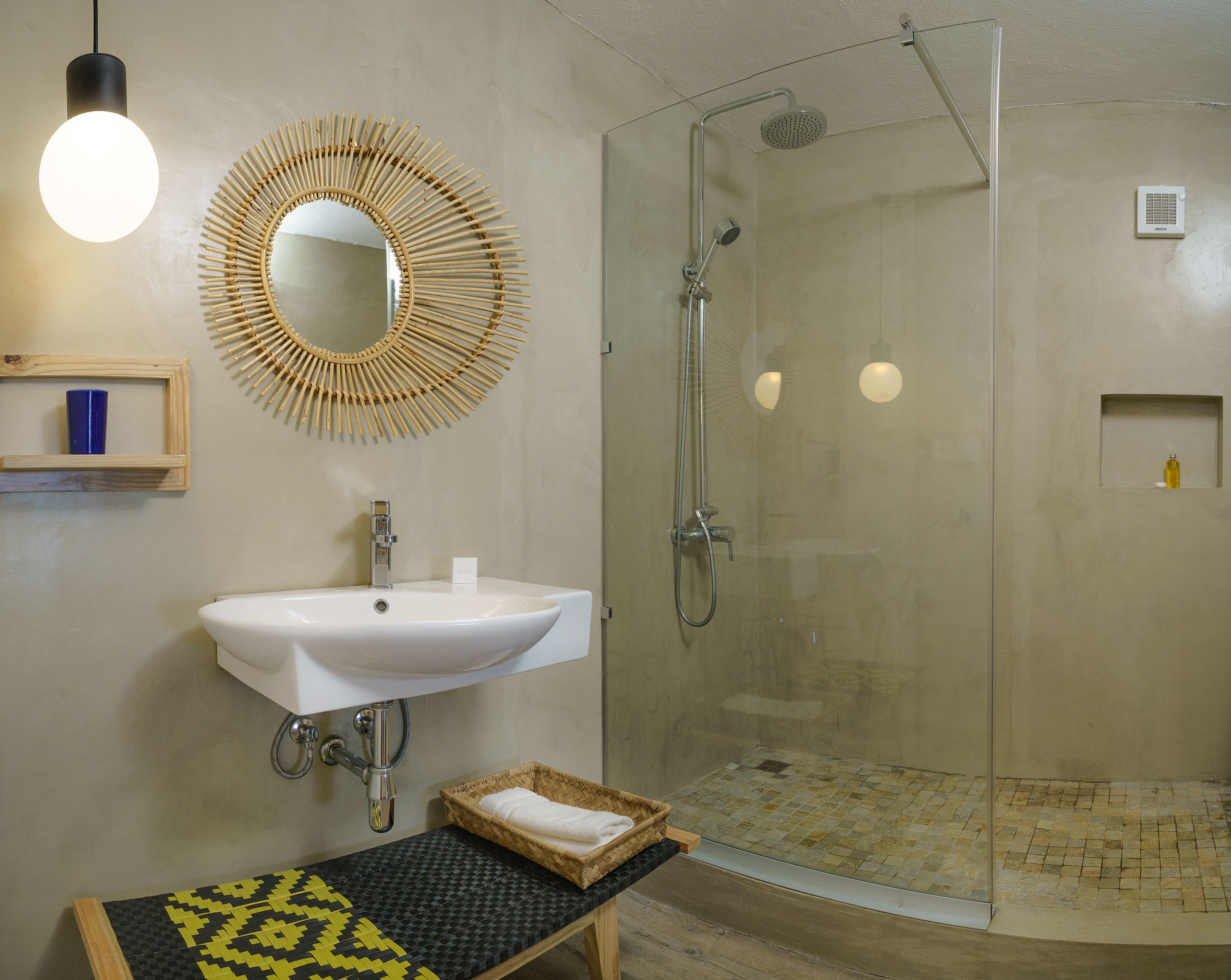 A bathroom with a white sink, a mirror, a shower, and a small shelf with a blue container.