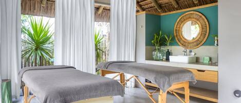 A spa room with two massage tables, a wooden ceiling, and a large mirror.