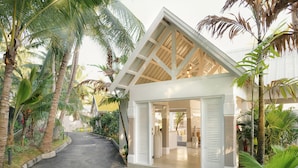 Una casa moderna con techo inclinado y puertas abiertas, rodeada de exuberante vegetación tropical.