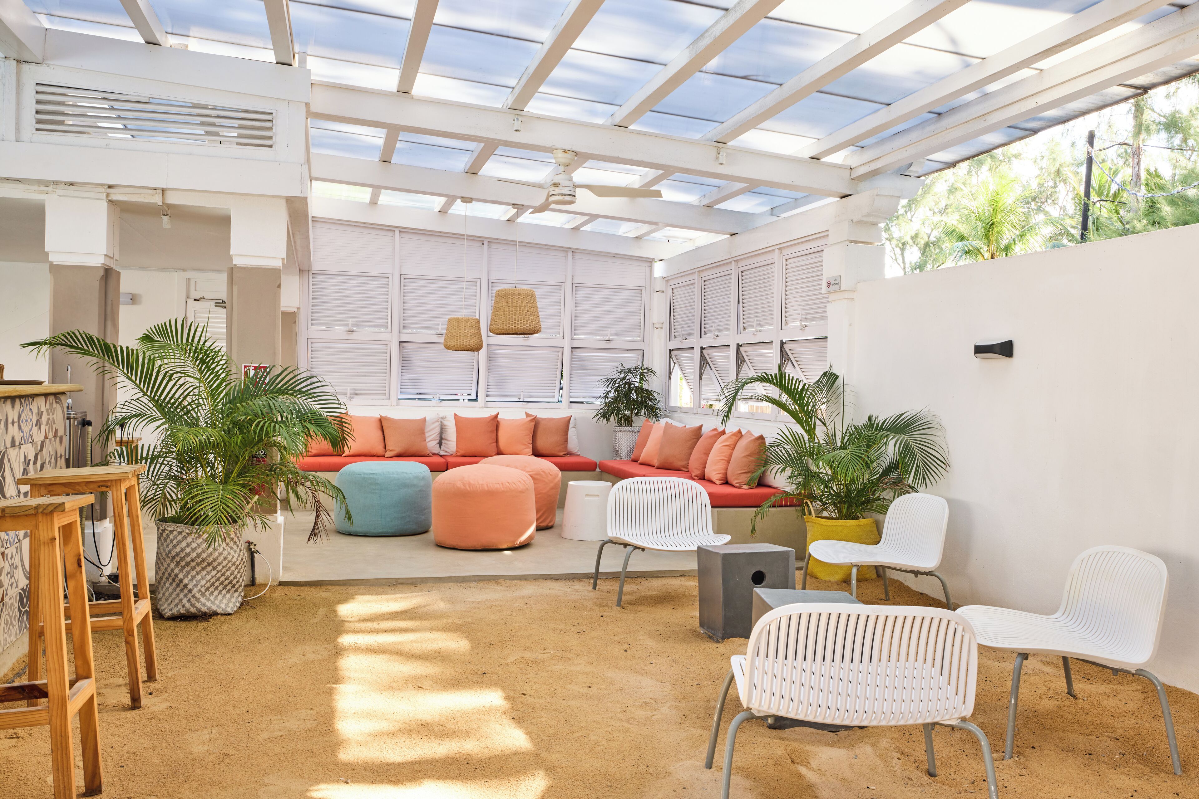 A sunlit interior with a wooden table, a cushioned seating area, and potted plants.