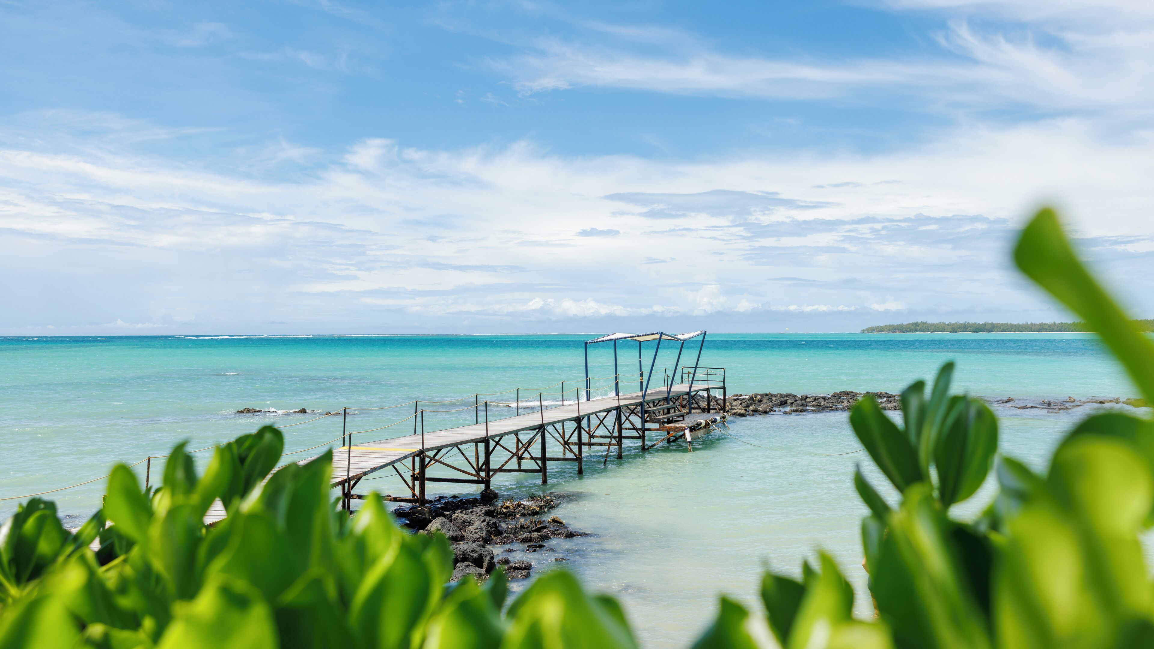 A wooden pier extending into turquoise waters, with a small shelter at the end.