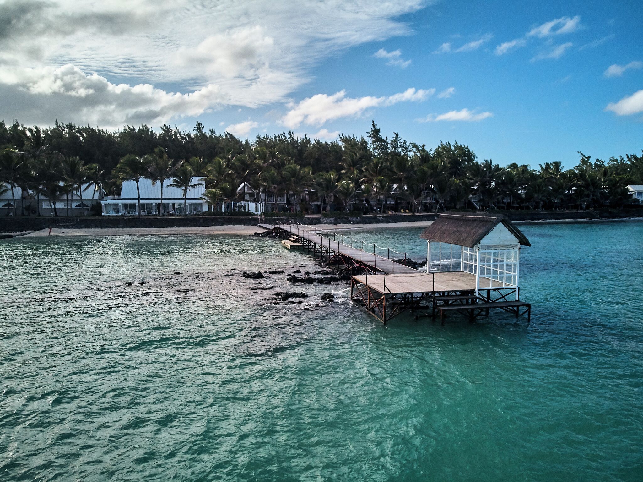Un muelle que se adentra en aguas turquesas con una estructura de techo de paja al final.